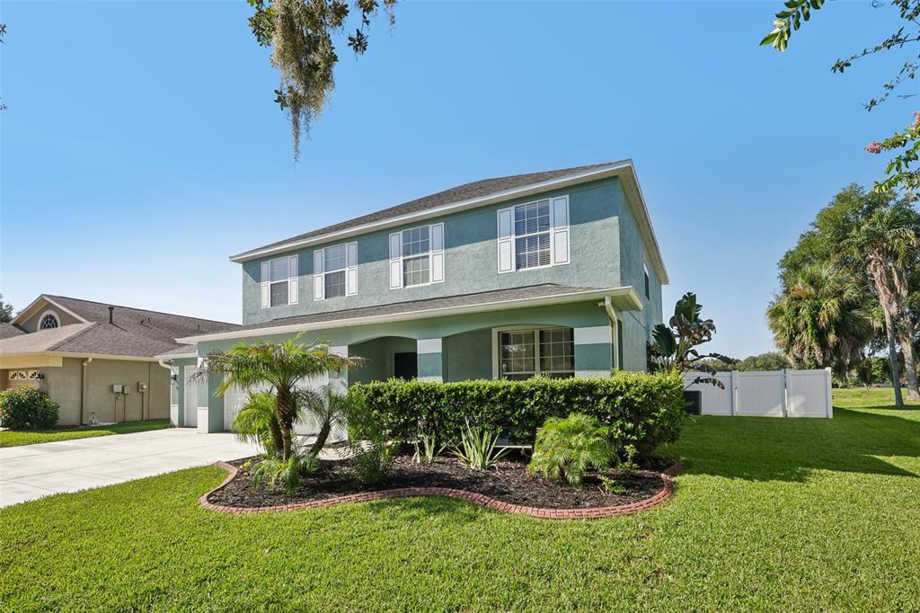 A two-story green house with a front lawn, landscaping, and a white fence — 205 ROSANA DRIVE, BRANDON, FL