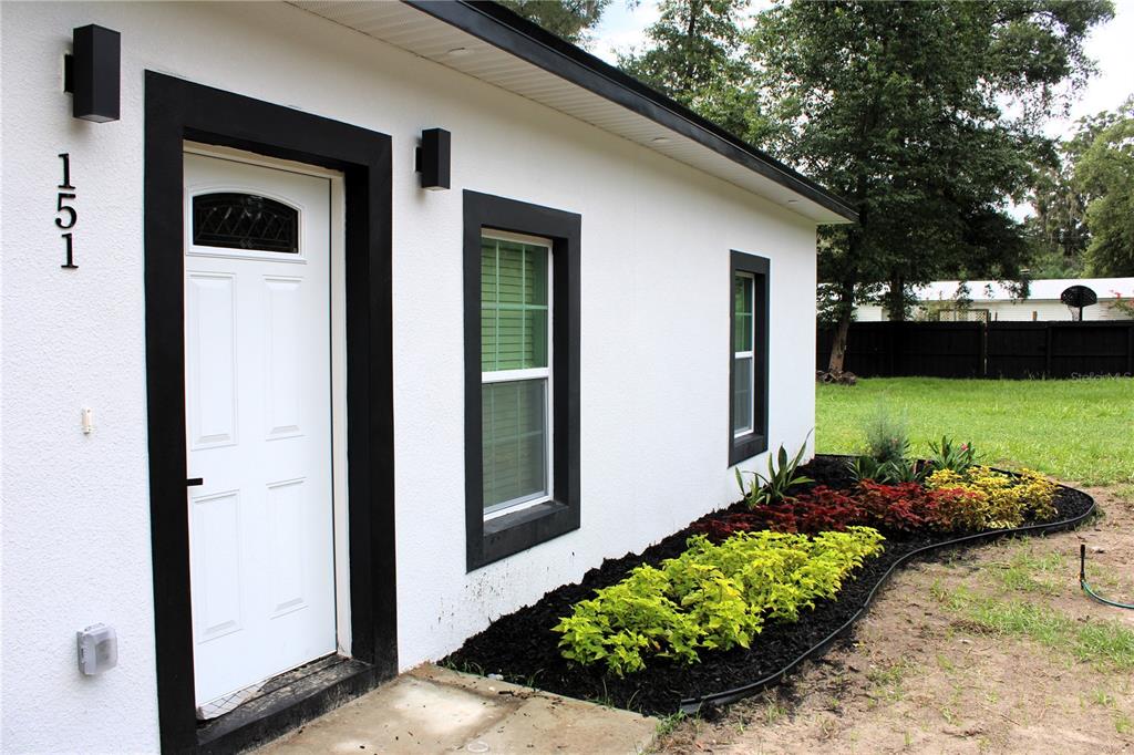 A white exterior wall with black trim, a front door, and a landscaped garden bed — 151 NW 133 COURT, OCALA, FL