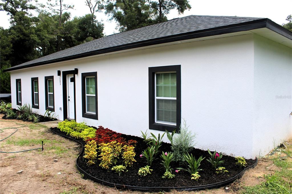 A white, single-story house with black trim and a landscaped garden bed in the front — 151 NW 133 COURT, OCALA, FL