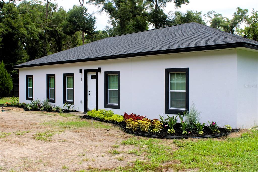 A white, single-story house with a dark roof and black window frames sits on a lot — 151 NW 133 COURT, OCALA, FL