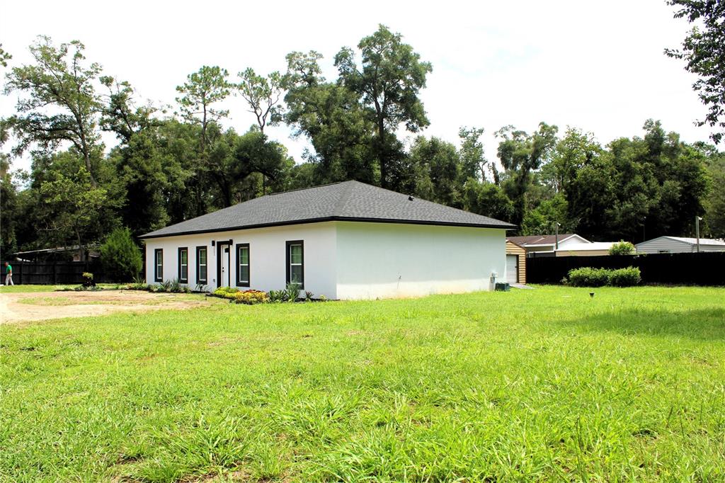 A white, single-story house with a dark roof sits on a large, grassy lot — 151 NW 133 COURT, OCALA, FL