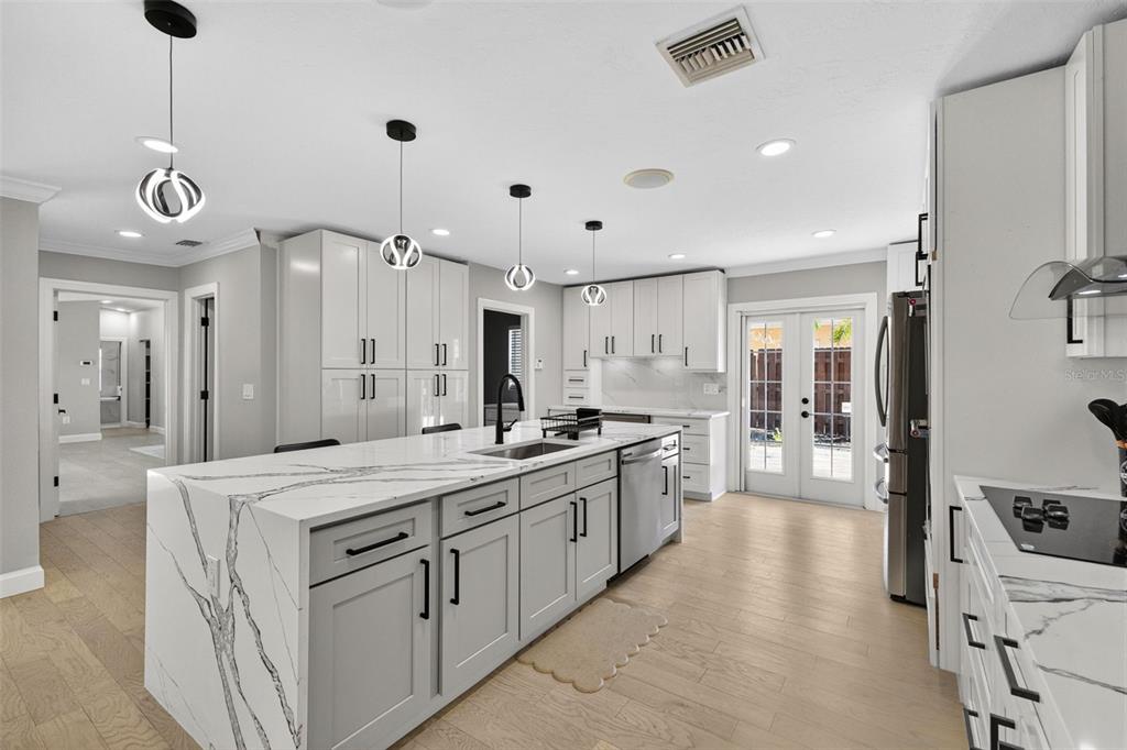 A modern kitchen features a large marble-topped island, gray cabinetry, and light wood flooring — 5073 HIGEL AVENUE, SARASOTA, FL
