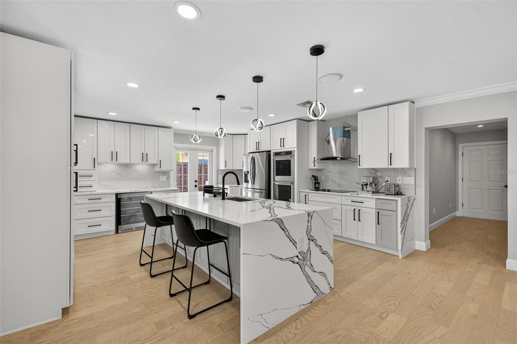A modern kitchen features white cabinetry, a marble-patterned waterfall island, and light wood flooring — 5073 HIGEL AVENUE, SARASOTA, FL