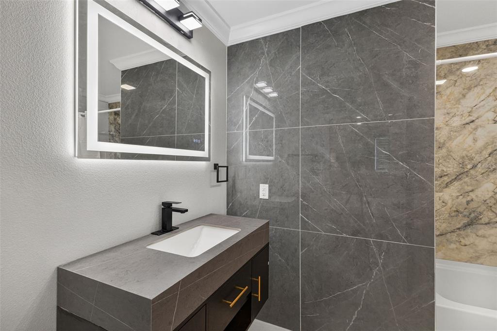 A modern bathroom features a dark vanity, a backlit mirror, and grey marble-look wall tiles — 5073 HIGEL AVENUE, SARASOTA, FL