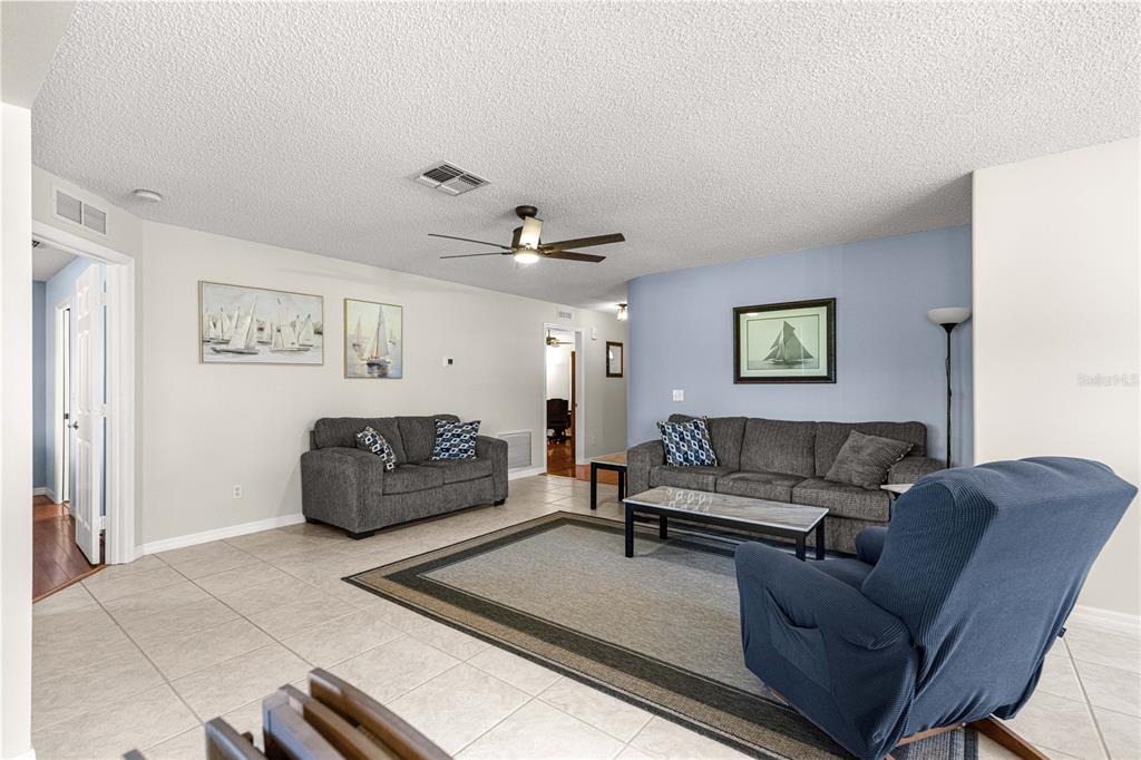 A living room features tile flooring, two gray sofas, a blue recliner, and nautical wall art — 9037 SW 91ST CIRCLE, OCALA, FL