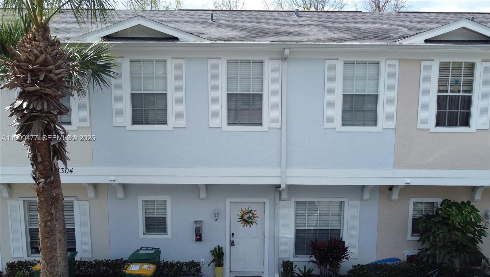 A two-story townhouse exterior features light blue siding, white shutters, and a front entrance — 3304 Lisa Ln # 102, Naples FL 34109, NAPLES, FL