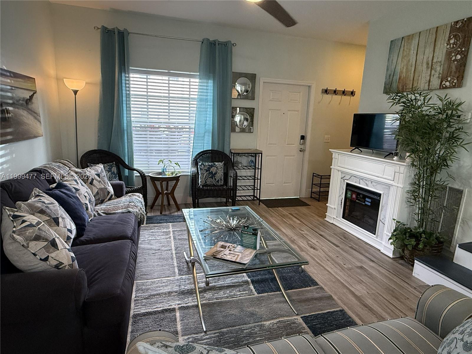 A living room features a dark sofa, glass coffee table, fireplace, and blue curtains — 3304 Lisa Ln # 102, Naples FL 34109, NAPLES, FL