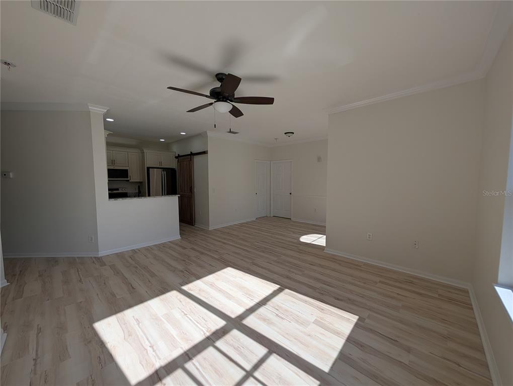 An open-concept living area features light wood-look flooring, a ceiling fan, and an adjacent kitchen — 2107 PORTOFINO PLACE UNIT 30-302, PALM HARBOR, FL