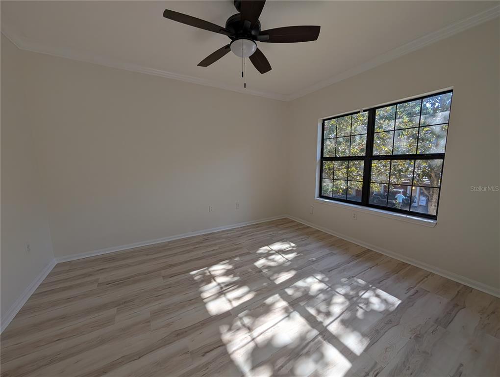 An empty bedroom features light wood-look flooring, a ceiling fan, and a large window — 2107 PORTOFINO PLACE UNIT 30-302, PALM HARBOR, FL