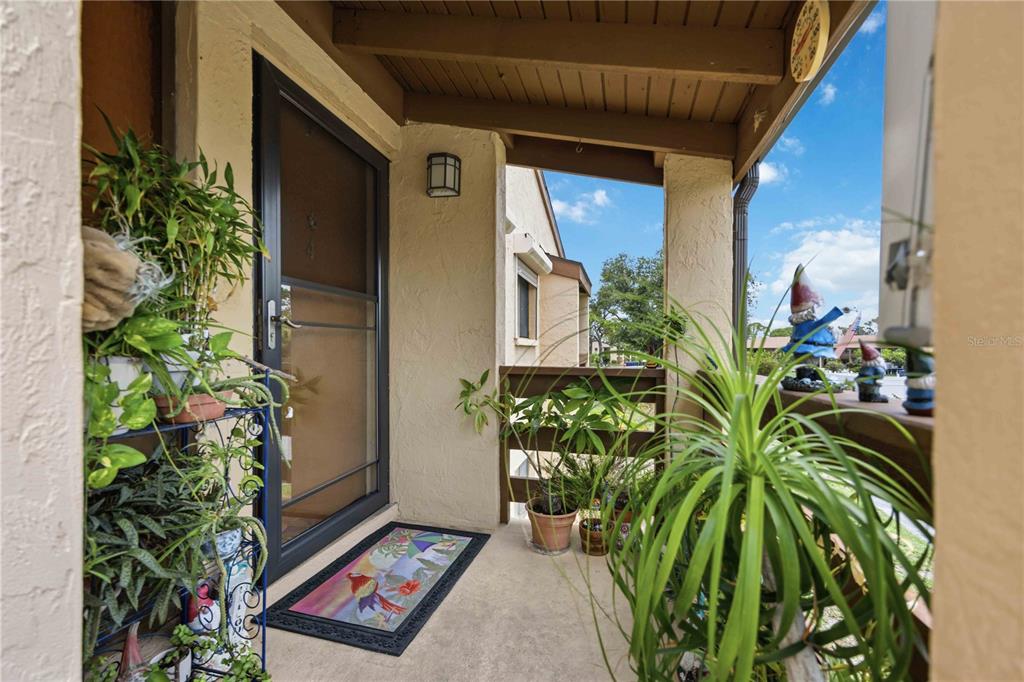 A covered porch features a dark screen door, potted plants, and a decorative welcome mat — 18 QUAILS RUN BOULEVARD UNIT 18202, ENGLEWOOD, FL