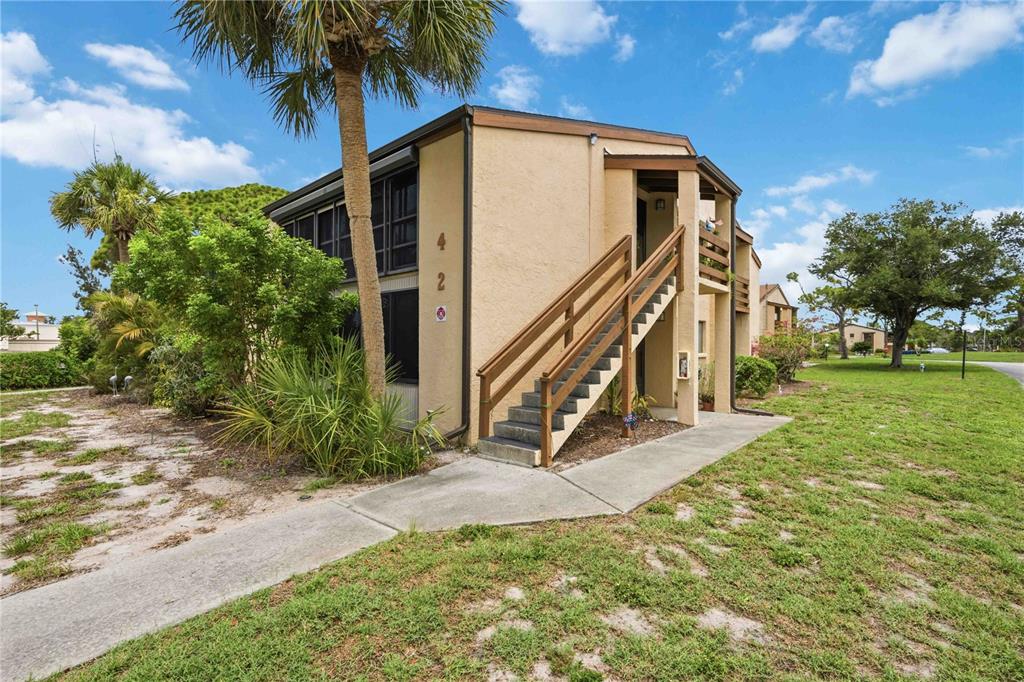A two-story tan apartment building with an exterior wooden staircase and a palm tree — 18 QUAILS RUN BOULEVARD UNIT 18202, ENGLEWOOD, FL