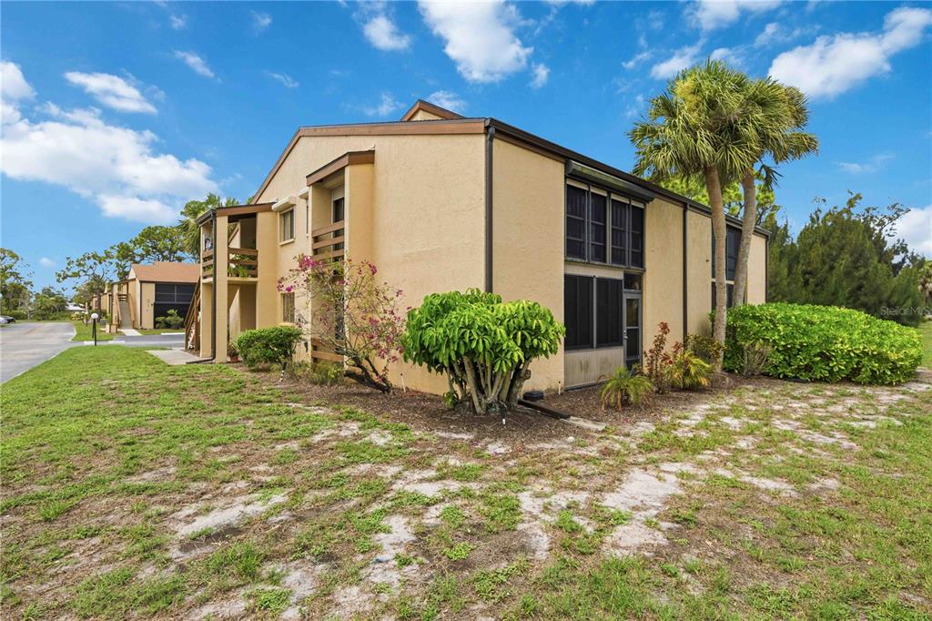 A two-story tan apartment building with a screened-in patio and a palm tree outside — 18 QUAILS RUN BOULEVARD UNIT 18202, ENGLEWOOD, FL