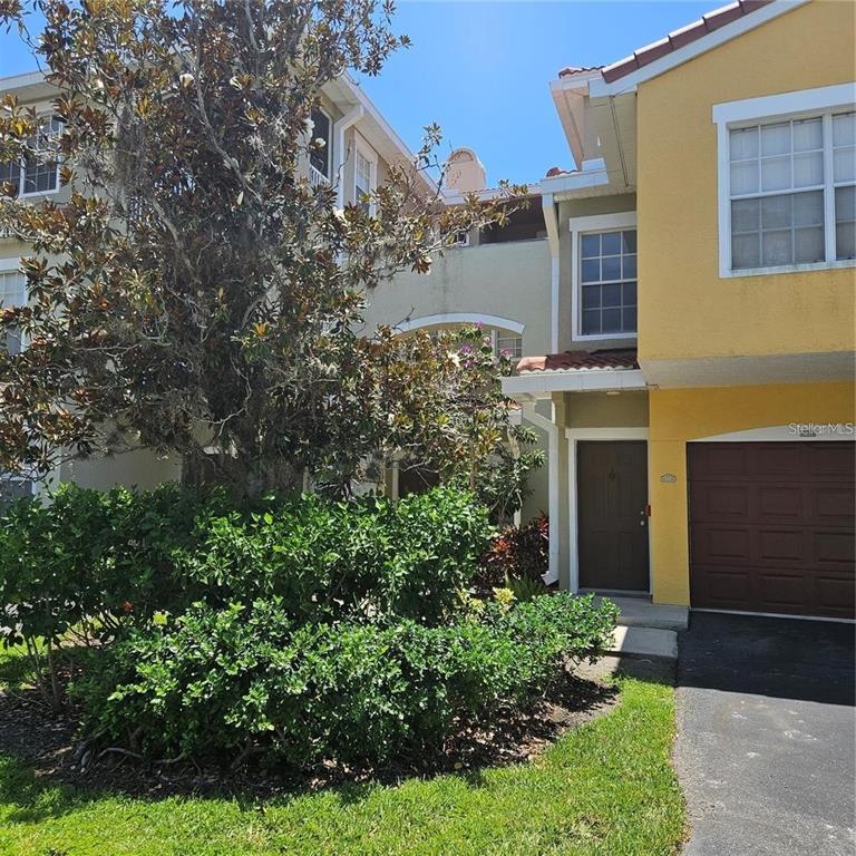 A two-story townhouse exterior features a yellow facade, a brown garage door, and landscaping — 5500 BENTGRASS DRIVE UNIT 6-112, SARASOTA, FL