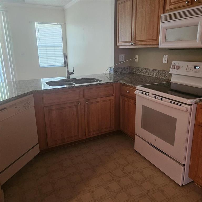 A kitchen features wood cabinets, granite countertops, white appliances, and a double-basin sink — 5500 BENTGRASS DRIVE UNIT 6-112, SARASOTA, FL