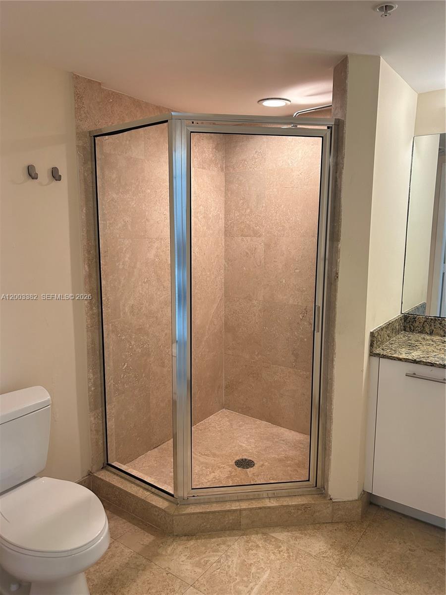 A bathroom features a corner shower stall with a glass door and beige stone tiles — 41 SE 5th St # 1108, Miami FL 33131, MIAMI, FL