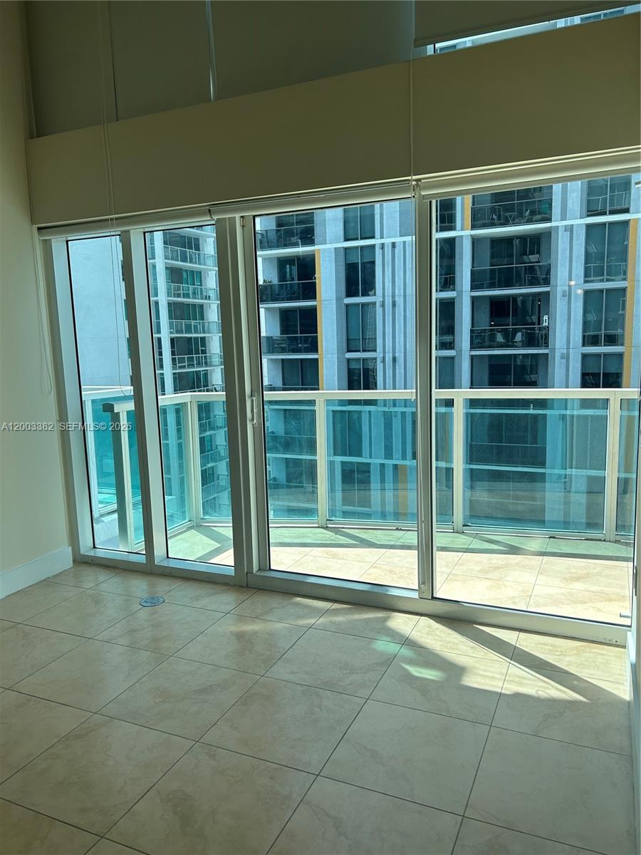 A room with light-colored tile flooring features floor-to-ceiling windows overlooking a balcony and buildings — 41 SE 5th St # 1108, Miami FL 33131, MIAMI, FL