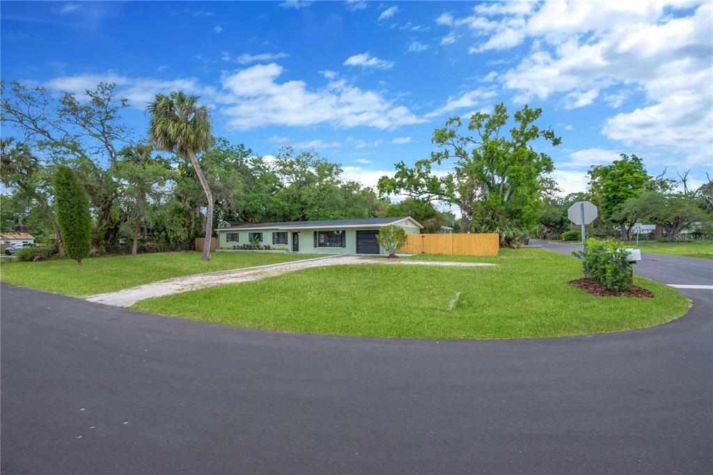 A single-story light green house with a gravel driveway and wooden fence sits on a lawn — 7502 LONE STAR PLACE, RIVERVIEW, FL