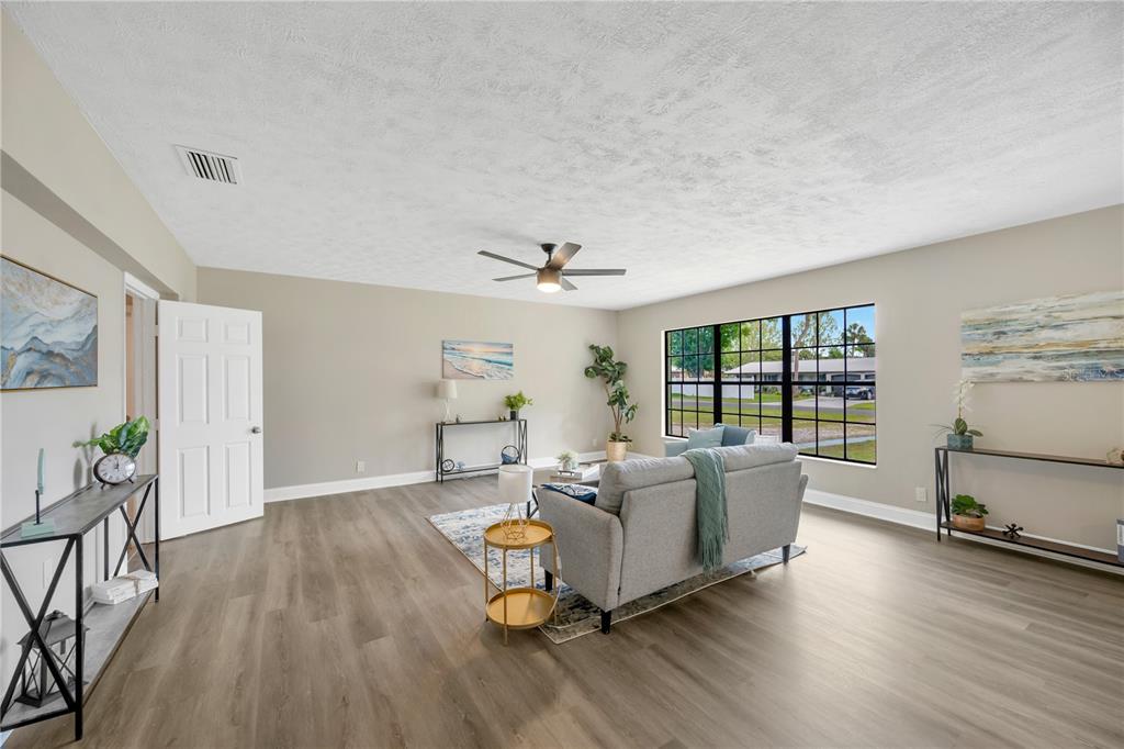 A living room with light wood-look flooring, a grey sofa, and large windows — 7502 LONE STAR PLACE, RIVERVIEW, FL