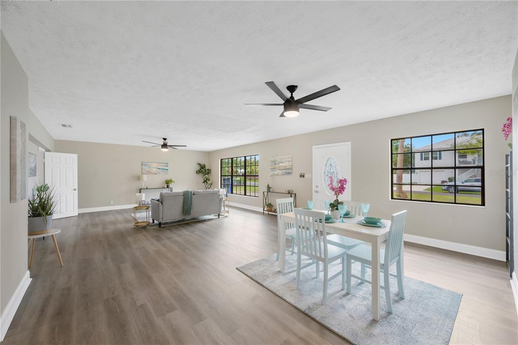 An open-concept living and dining area with light wood flooring, ceiling fans, and large windows — 7502 LONE STAR PLACE, RIVERVIEW, FL