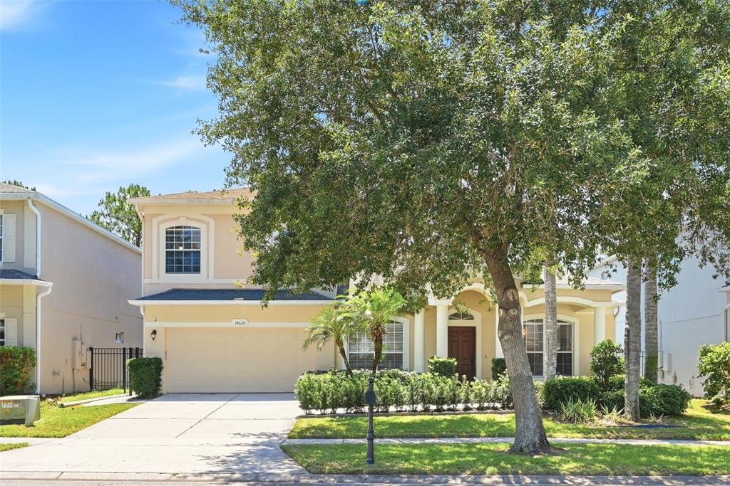 A two-story suburban house with a beige stucco exterior, a two-car garage, and large trees — 14620 CABLESHIRE WAY, ORLANDO, FL