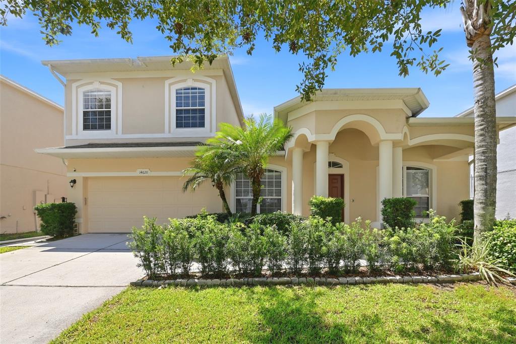 A two-story suburban house with a beige stucco exterior, a two-car garage, and landscaping — 14620 CABLESHIRE WAY, ORLANDO, FL
