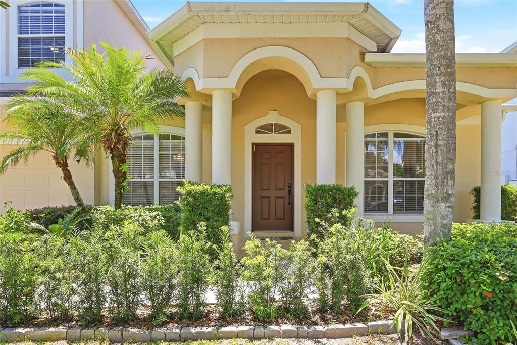 The exterior of a tan house features a brown front door, white columns, and landscaping — 14620 CABLESHIRE WAY, ORLANDO, FL