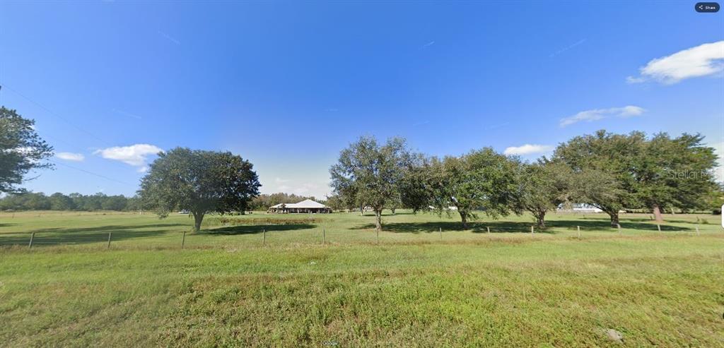 A wide, grassy field with a line of trees and a house in the distance — OLD GRADE RD, POLK CITY, FL