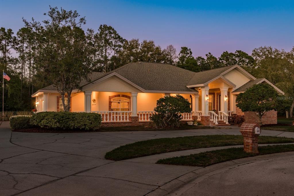 A single-story house with a brick-trimmed porch and a circular driveway at dusk — 6207 CLAIRE DE LUNE COURT, NEW PORT RICHEY, FL