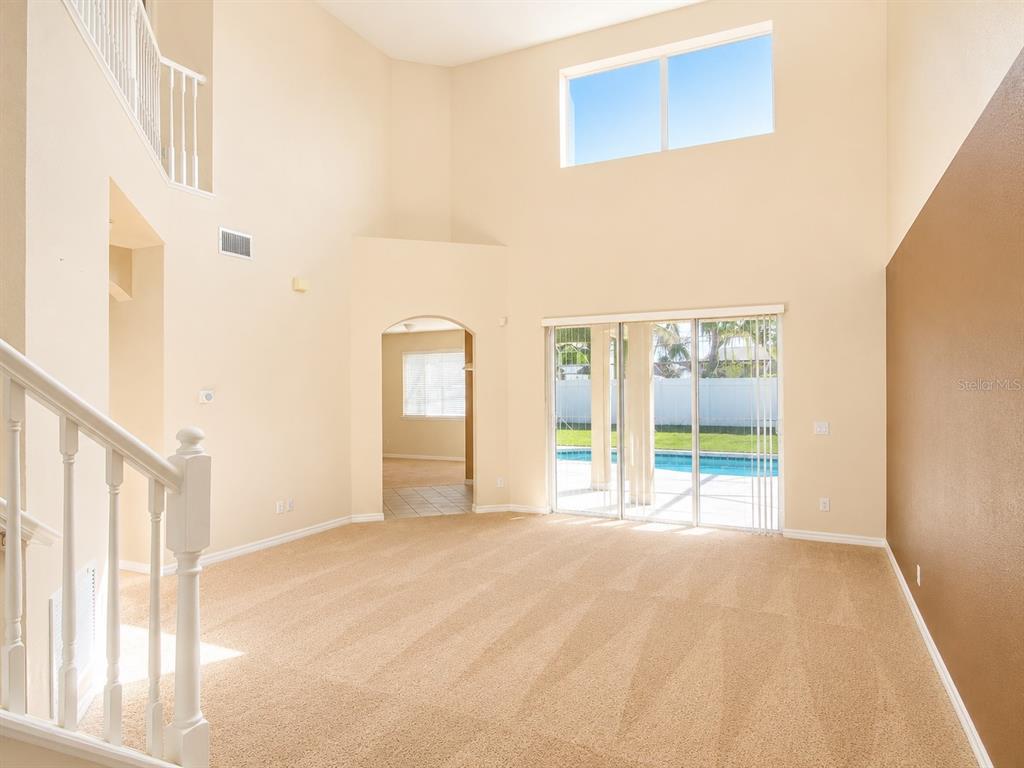 A carpeted living room with high ceilings, a staircase, and sliding doors leading to a pool — 1460 EQUINOX CIRCLE, SANFORD, FL