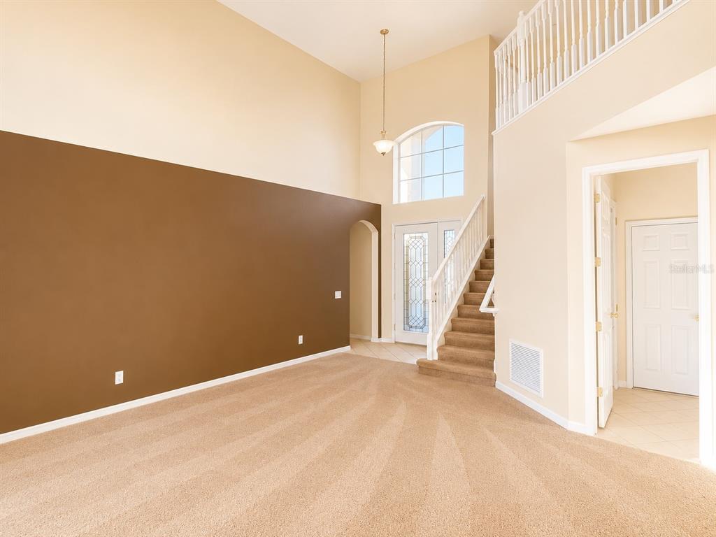 A living room with high ceilings, a brown accent wall, and a staircase with railing — 1460 EQUINOX CIRCLE, SANFORD, FL