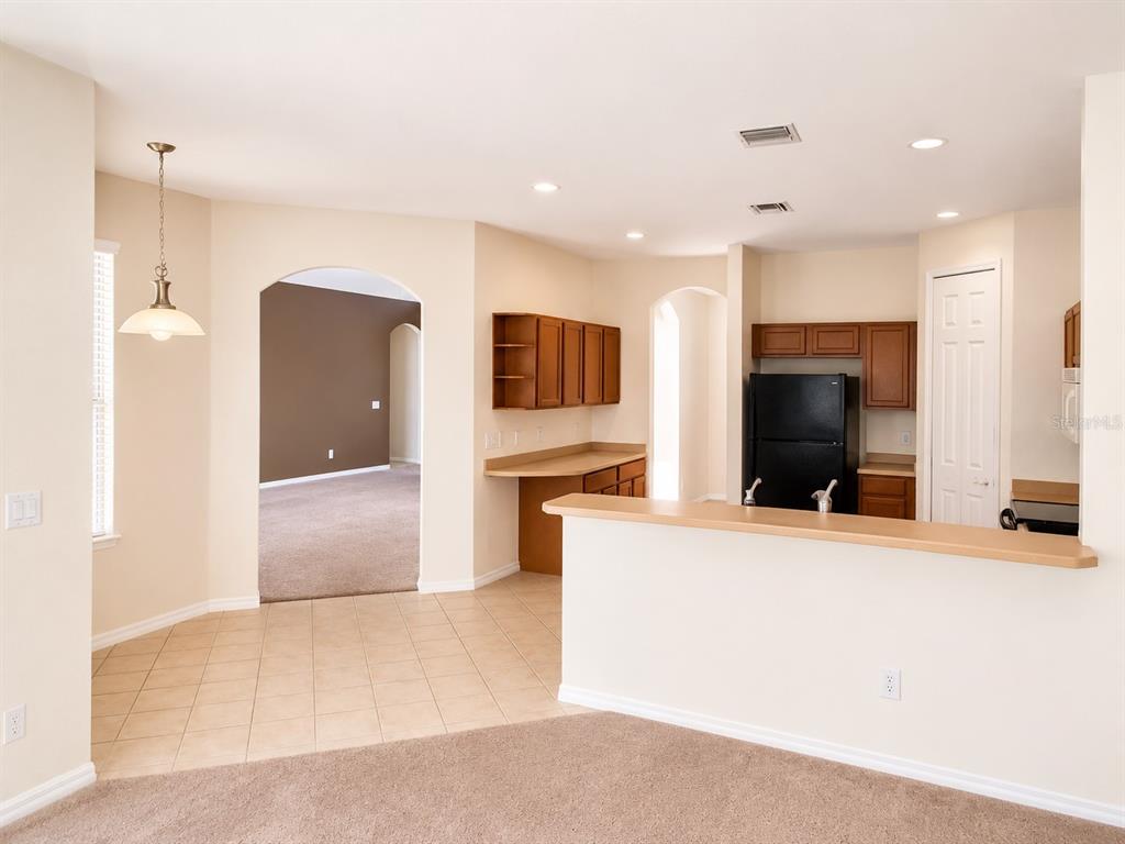 A kitchen with light wood cabinets, a breakfast bar, and tile flooring overlooks a carpeted room — 1460 EQUINOX CIRCLE, SANFORD, FL