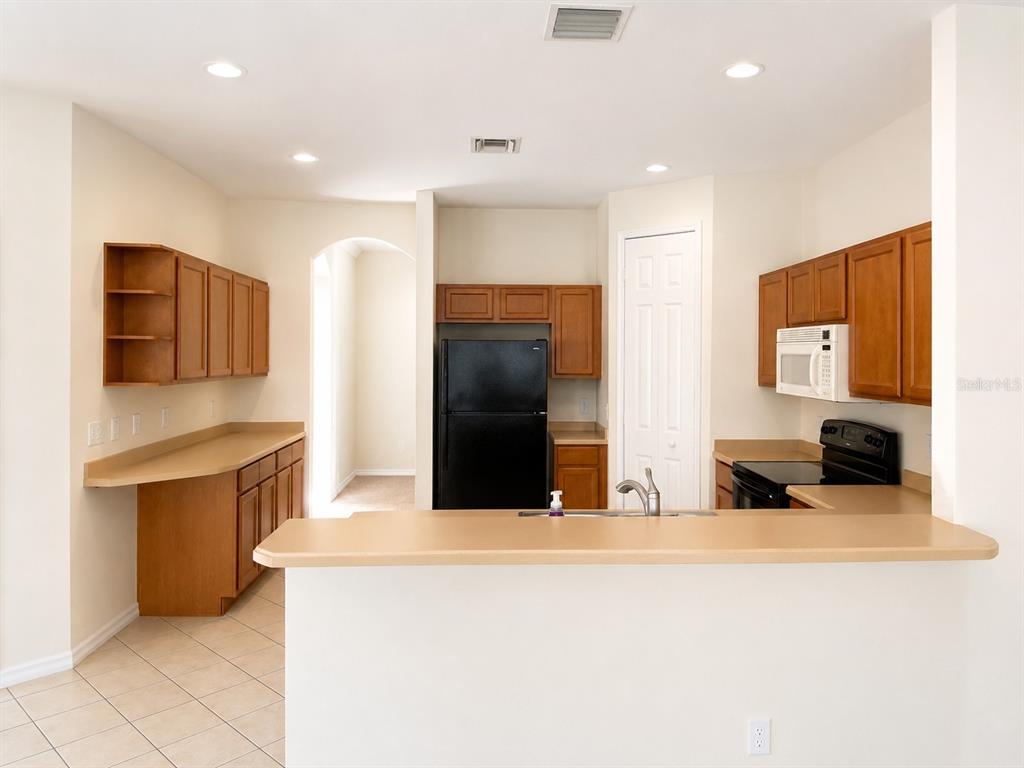 A kitchen with wood cabinets, black appliances, and a breakfast bar overlooking the room — 1460 EQUINOX CIRCLE, SANFORD, FL
