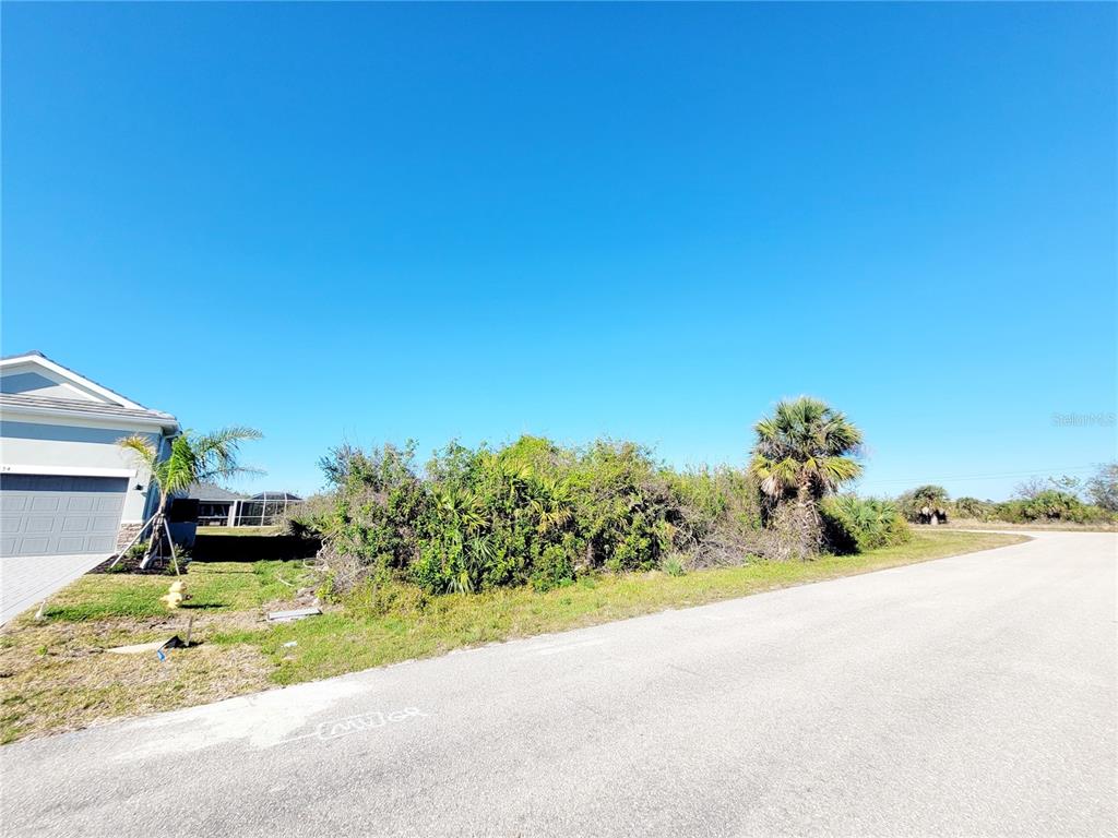 A vacant, overgrown lot sits next to a residential house along a paved street — 14442 AMESTOY AVENUE, PORT CHARLOTTE, FL