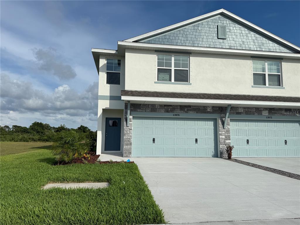 A two-story townhouse exterior features a light-blue garage door, stone accents, and a blue door — 13978 EMERALD FIELDS DRIVE Lot 25, HUDSON, FL