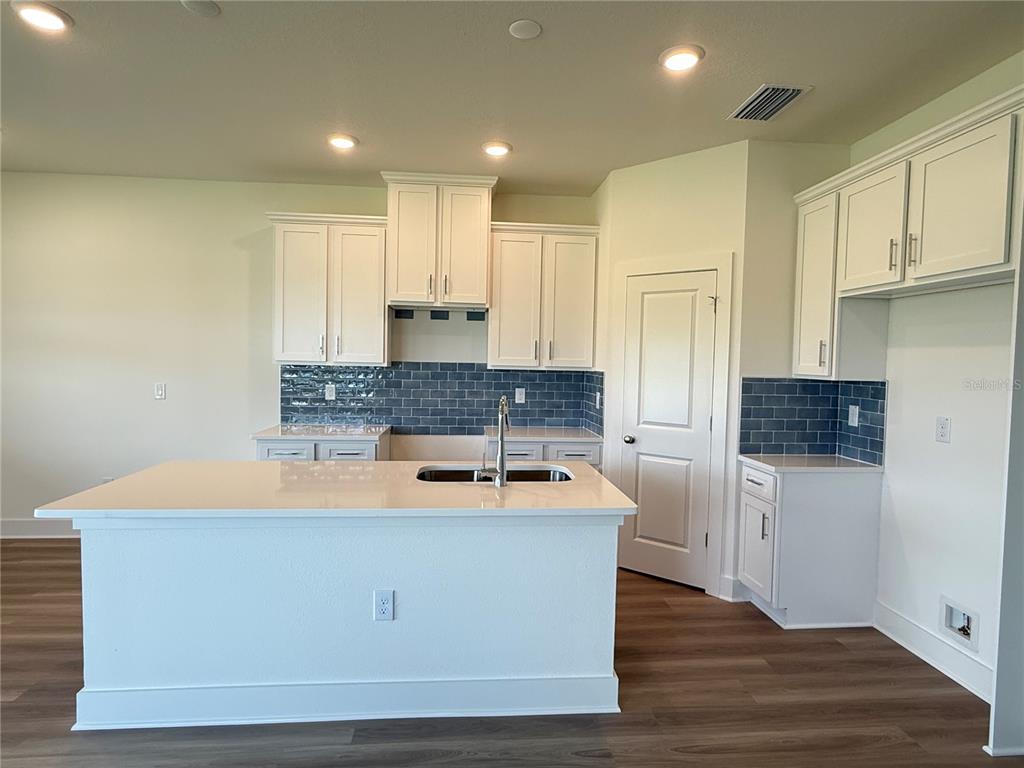A kitchen features white cabinets, a quartz-topped island, and a blue subway tile backsplash — 13978 EMERALD FIELDS DRIVE Lot 25, HUDSON, FL