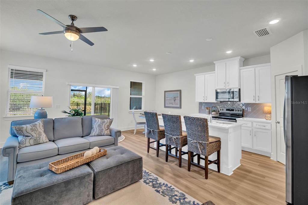 An open-concept kitchen and living area features white cabinetry, a kitchen island, and gray furniture — 13978 EMERALD FIELDS DRIVE Lot 25, HUDSON, FL