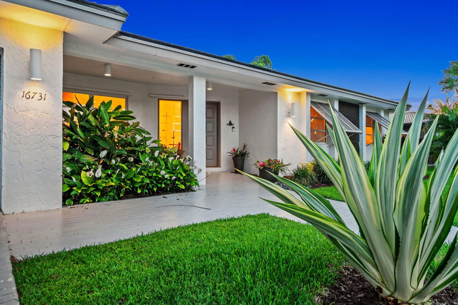 A white single-story house exterior features a covered entryway, lush landscaping, and a green lawn — 16731 Harbor Court, Weston FL 33326, WESTON, FL