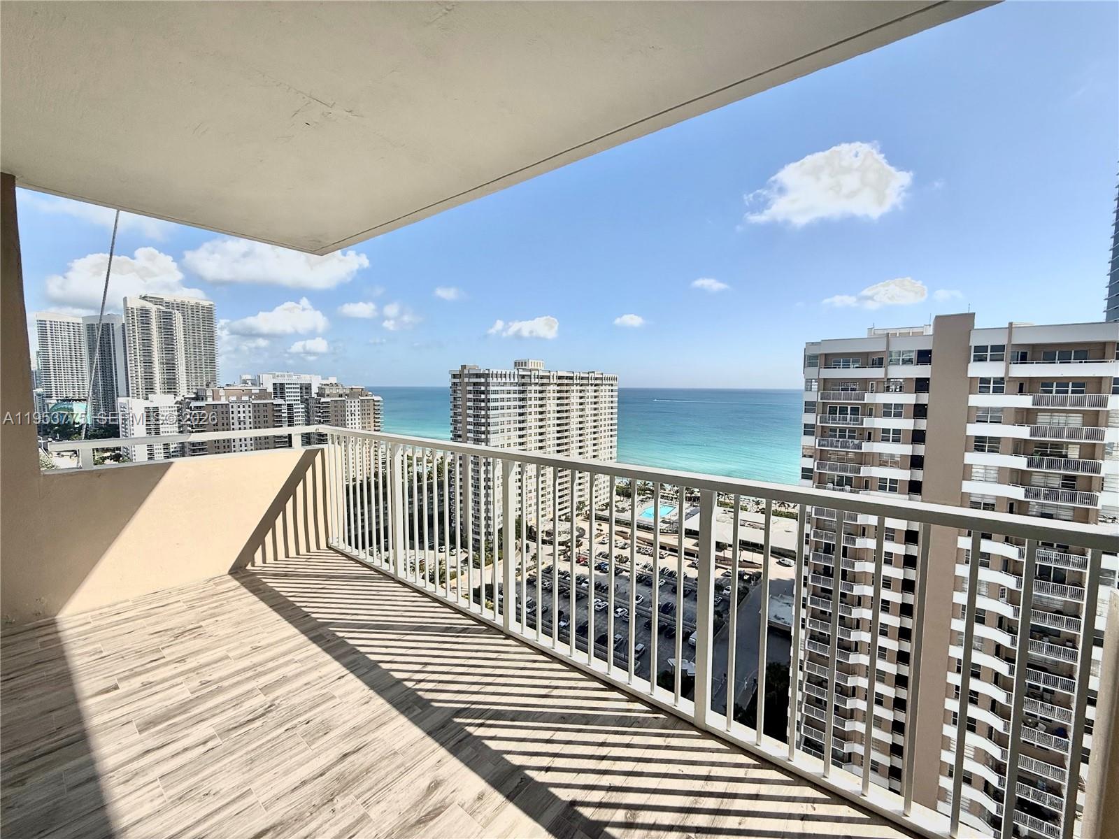 A high-rise balcony with wood-look tile flooring overlooks a parking lot and the ocean — 1985 S Ocean Dr # 22P, Hallandale Beach FL 33009, HALLANDALE BEACH, FL