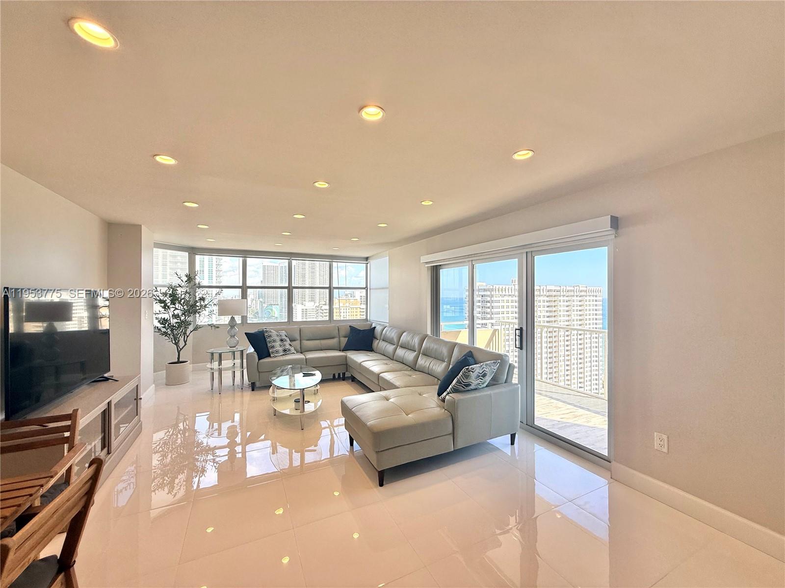A bright living room features a large sectional sofa, tile flooring, and a balcony view — 1985 S Ocean Dr # 22P, Hallandale Beach FL 33009, HALLANDALE BEACH, FL