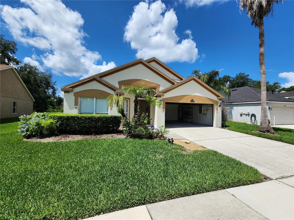 A single-story house with a beige stucco exterior, a two-car garage, and a manicured lawn — 30702 IVERSON DRIVE, WESLEY CHAPEL, FL