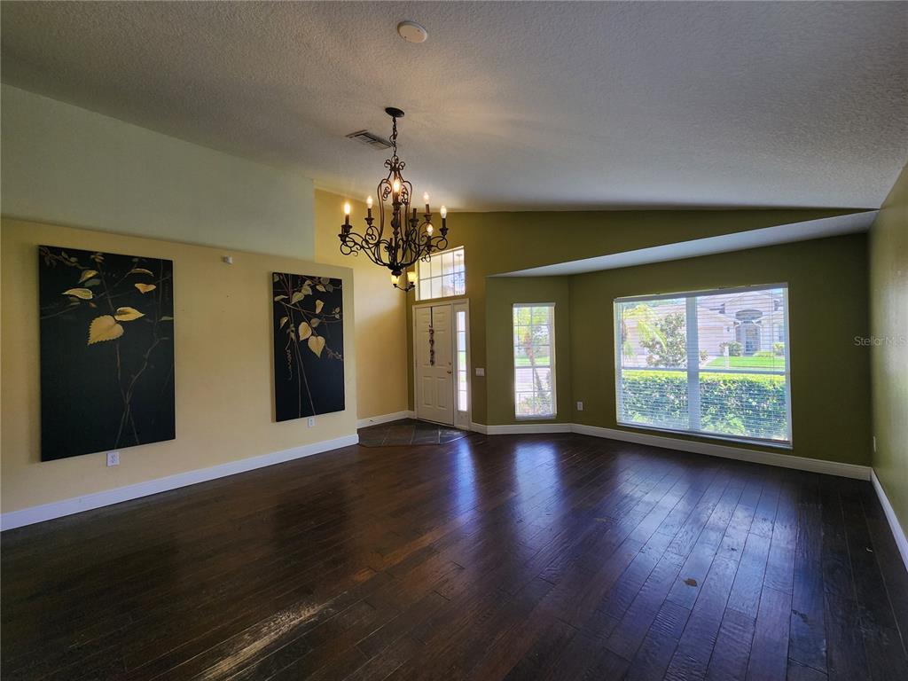 A spacious living room features dark wood floors, olive green walls, and a large chandelier — 30702 IVERSON DRIVE, WESLEY CHAPEL, FL