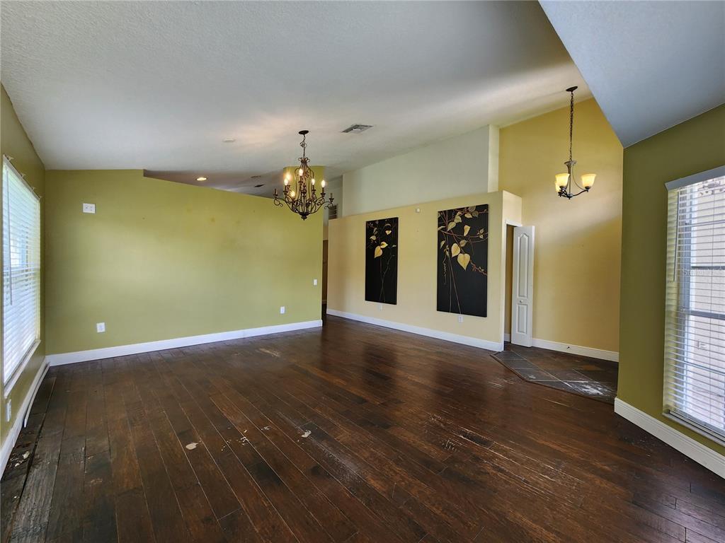 A spacious room with olive green walls, dark wood flooring, two chandeliers, and two wall paintings — 30702 IVERSON DRIVE, WESLEY CHAPEL, FL