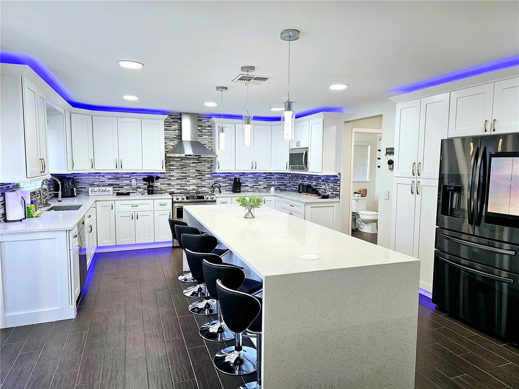 A modern kitchen features white cabinets, a large quartz island, black barstools, and blue lighting — 502 CANNA DRIVE, DAVENPORT, FL