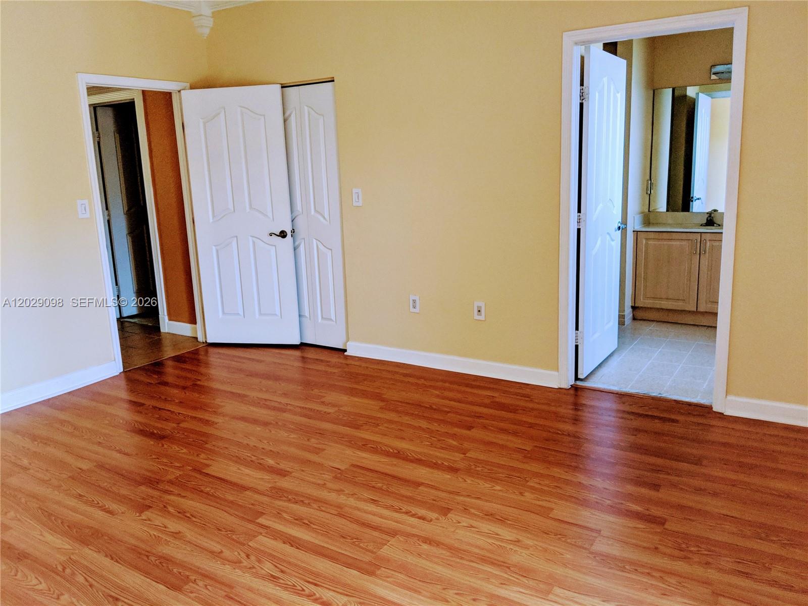 An empty room features yellow walls, wood-look flooring, two doorways, and a set of closet doors — 11262 SW 230th Ter # 11262, Miami FL 33170, MIAMI, FL