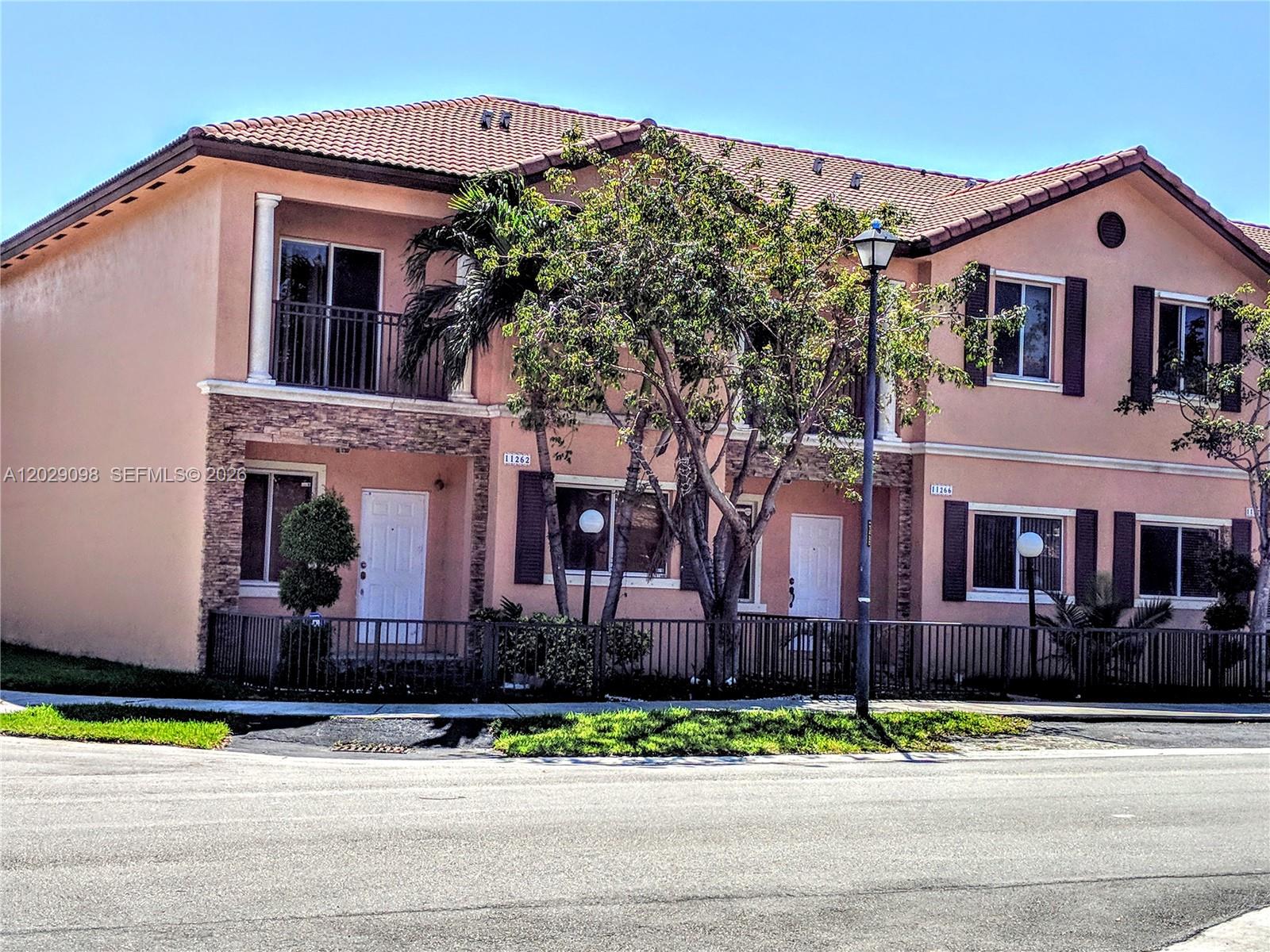 A two-story peach-colored townhouse features a tiled roof, stone accents, and a front fence — 11262 SW 230th Ter # 11262, Miami FL 33170, MIAMI, FL