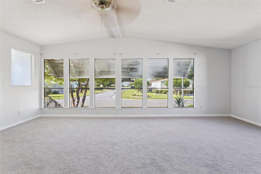 A spacious, carpeted living room features a vaulted ceiling and a wall of large windows — 1787 W SCHWARTZ BOULEVARD, LADY LAKE, FL