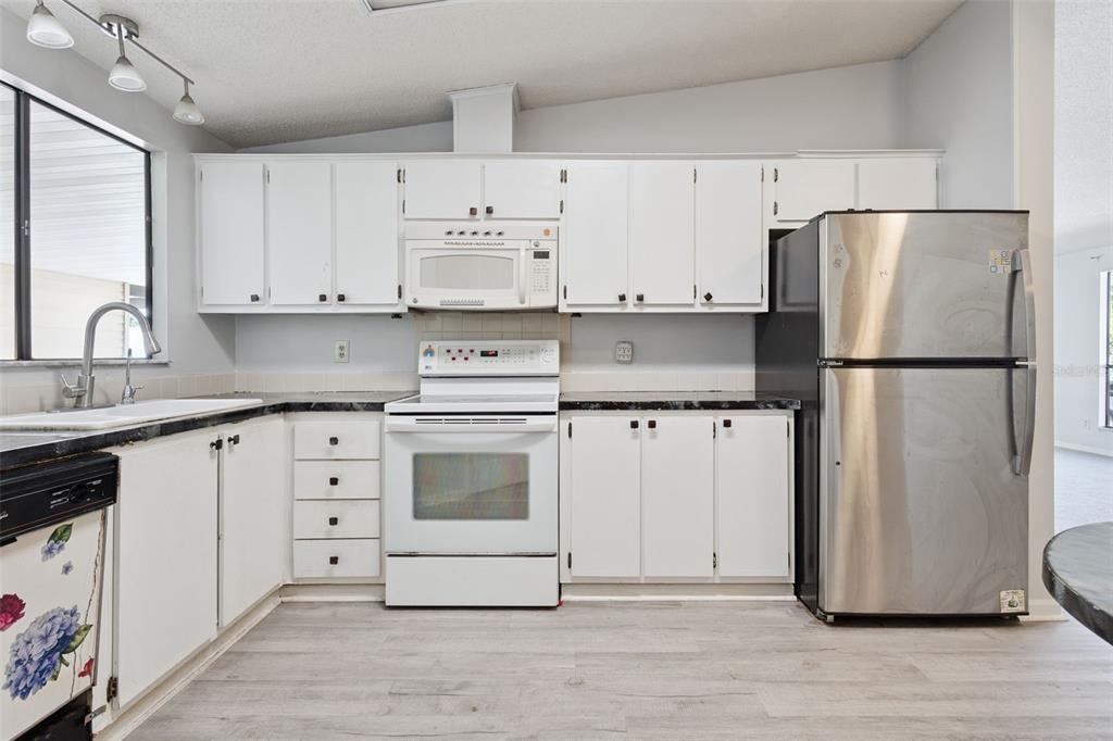A kitchen features white cabinets, a white stove, a stainless steel refrigerator, and light flooring — 1787 W SCHWARTZ BOULEVARD, LADY LAKE, FL