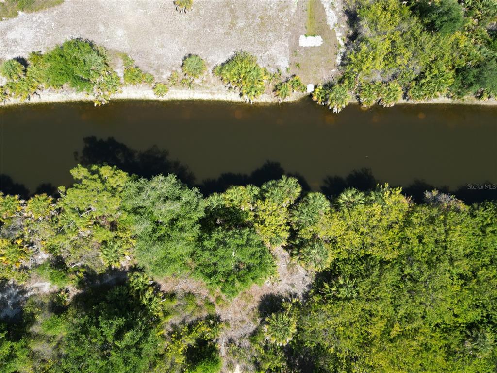 An aerial view shows a narrow canal bordered by dense trees and vegetation — 7418 SIOUX STREET, PORT CHARLOTTE, FL