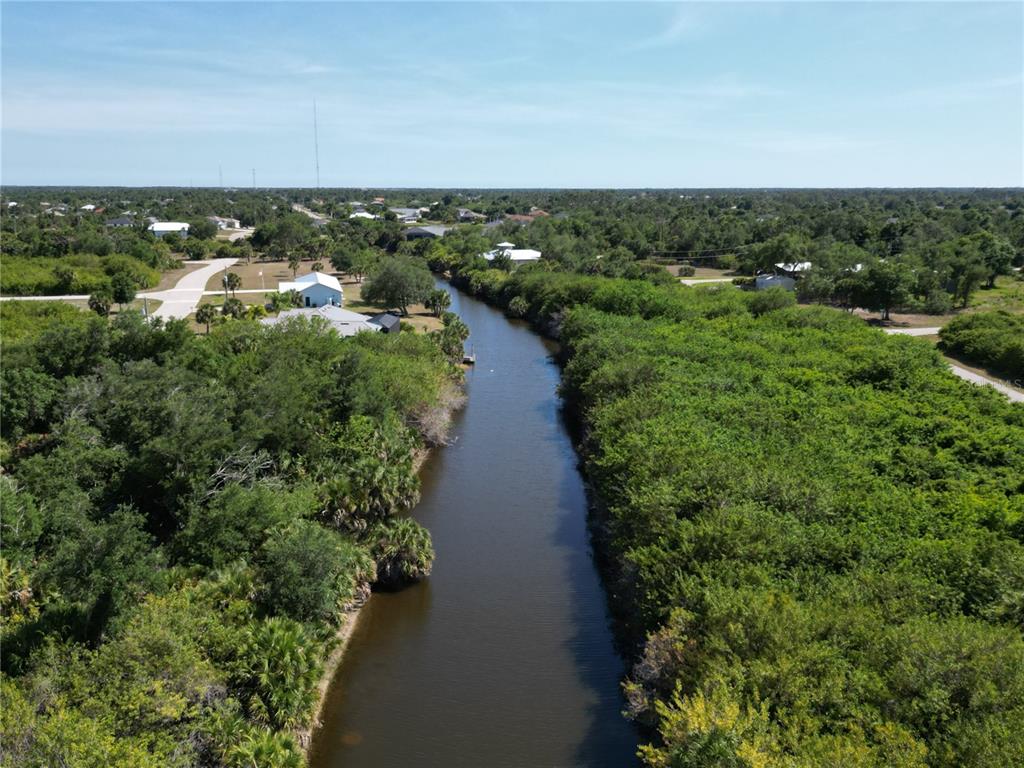 An aerial view shows a narrow canal winding through dense green vegetation and residential properties — 7418 SIOUX STREET, PORT CHARLOTTE, FL