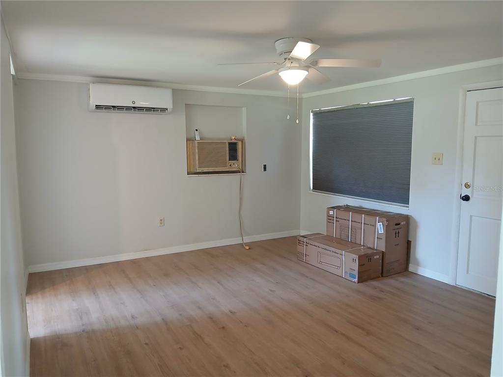 A room with light wood flooring, a ceiling fan, a wall-mounted AC unit, and boxes — 10424 E VICTORY LANE, INVERNESS, FL